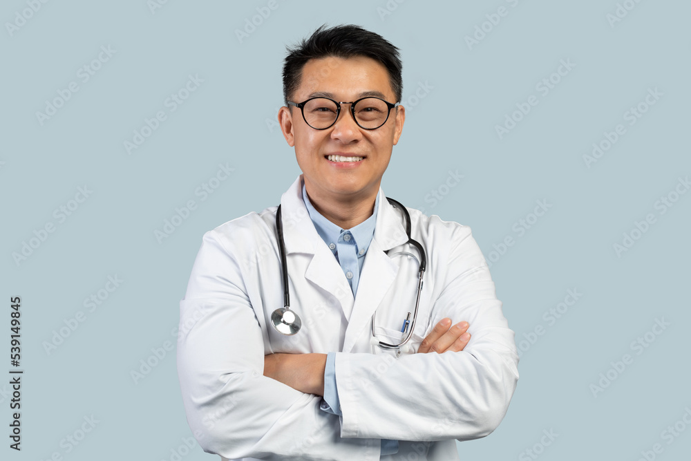 Cheerful middle aged chinese male doctor in white coat, glasses with crossed arms look at camera Cheerful middle aged chinese male doctor in white coat, glasses with crossed arms look at camera