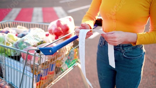 Close Up woman checks paper check after shopping for groceries at mall by checking Dear Amount bill in a grocery cart. increase in food prices, spending money in hypermarket. Woman checking grocery
