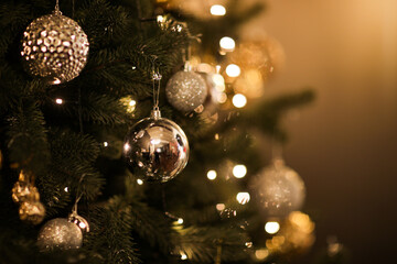 Close up view of beautiful fir branches with shiny golden bauble or ball, xmas ornaments and lights, Christmas holidays background. copy space. Decoration on christmas tree. Festive new 2023 year