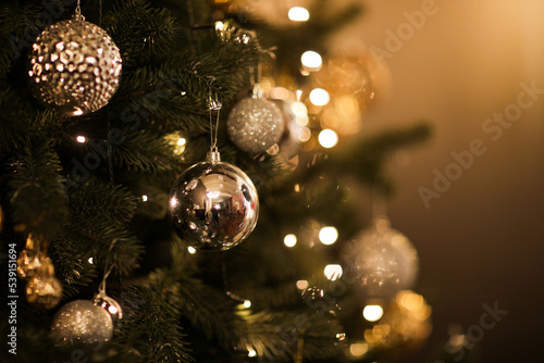 Close up view of beautiful fir branches with shiny golden bauble or ball, xmas ornaments and lights, Christmas holidays background. copy space. Decoration on christmas tree. Festive new 2023 year