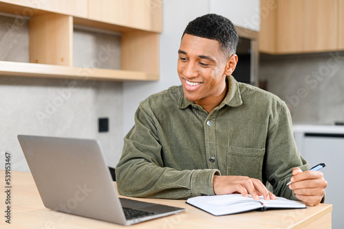 Concentrated latin student looking at the laptop display, solving business tasks, looking for new ideas while writing something at the notebook. People and technologies concept