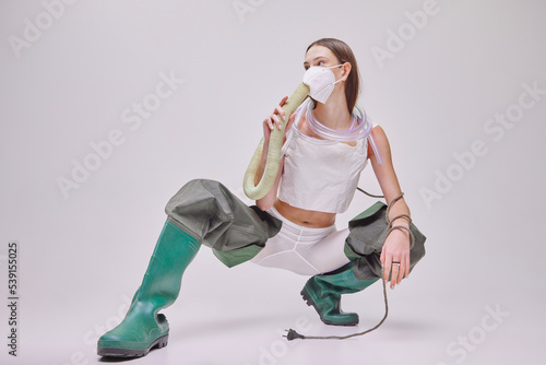 Portrait of young beautiful girl in rubber boots, vacuum cleaner on back and mask isolated on grey background. Fresh air photo