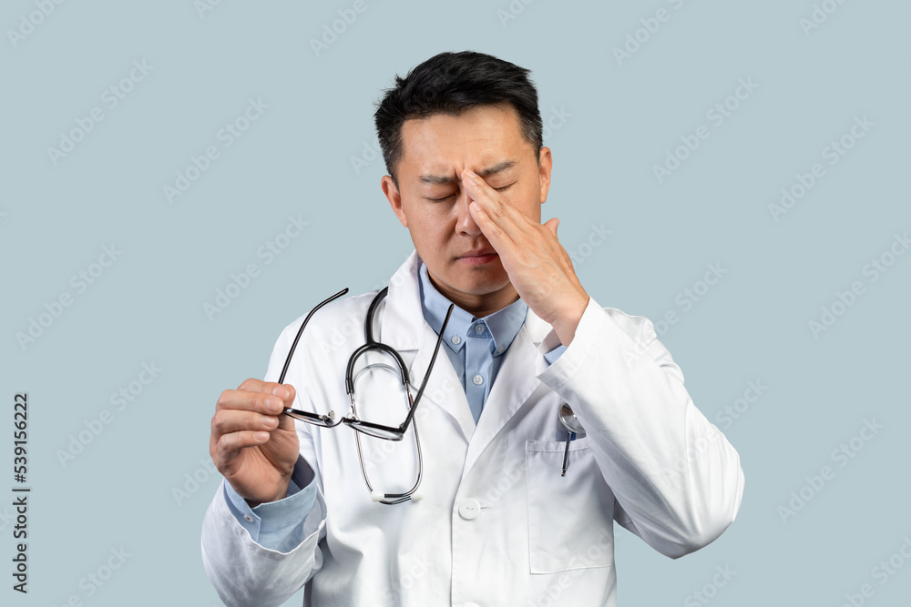 Tired sad middle aged chinese man doctor in white coat takes off glasses, rubs eyes with hand Tired sad middle aged chinese man doctor in white coat takes off glasses, rubs eyes with hand