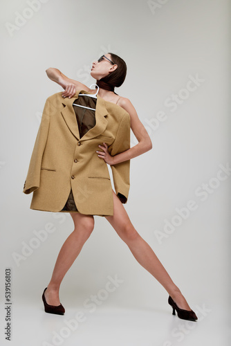 Portrait of stylish young girl posing in trendy singlasses, holding oversized jacket isolated over grey studio background photo