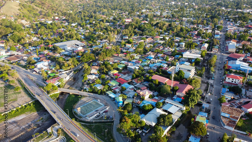 Aerial drone view of residential houses, inner city shops, businesses, and football pitch surrounded by green trees in capital of Dili, Timor-Leste in South East Asia