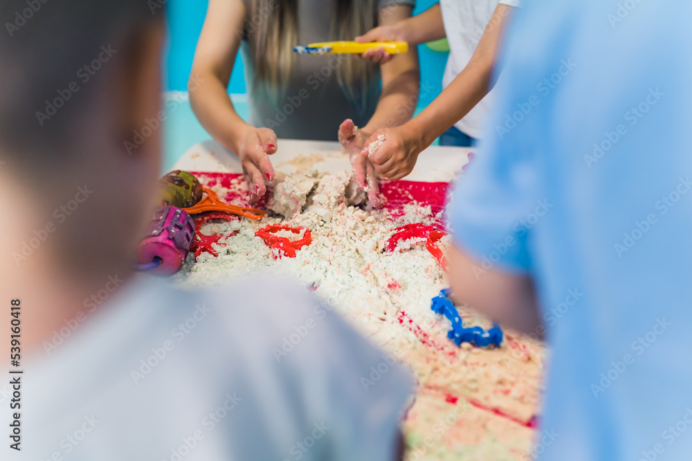a teacher and kids trying to make forms with kinetic sand, kindergarten closeup view . High quality photo