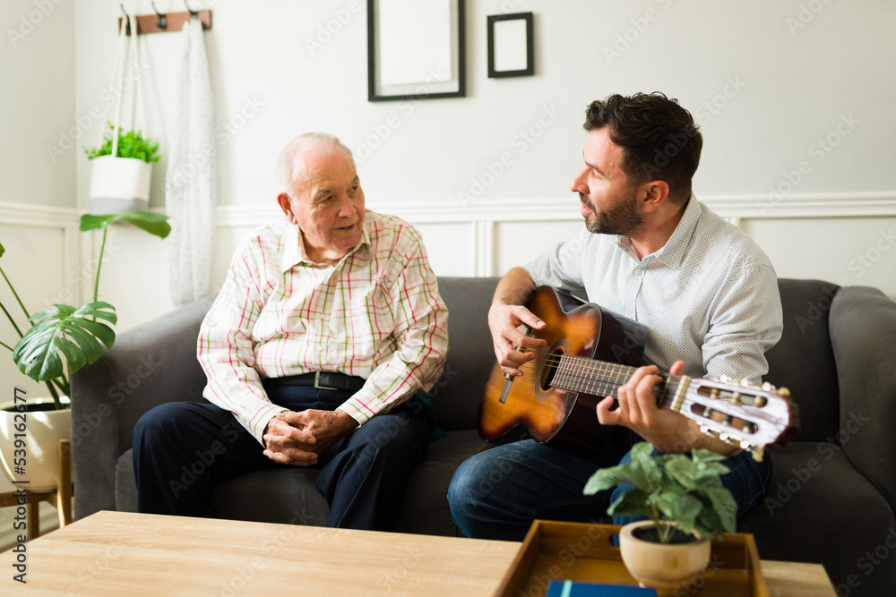 Cheerful son playing the guitar and enjoying music with his old father Cheerful son playing the guitar and enjoying music with his old father