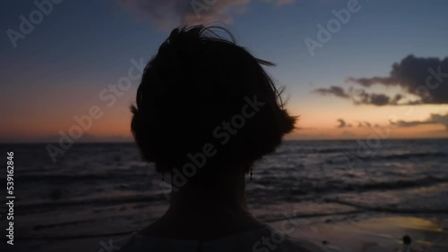 Silhouette from the back of girl dreaming at seaside in evening light. Woman relaxing meditating alone on ocean beach at colorful sunset sky background. Stress overcome. Film grain texture. Dolly.