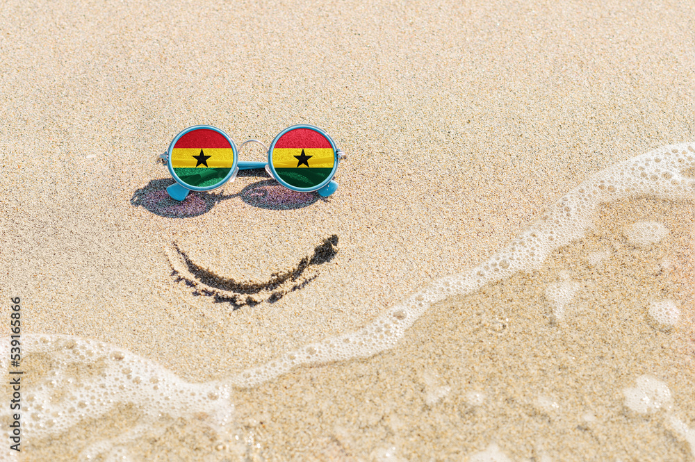 Obraz premium A painted smile on the sand and sunglasses with the flag of the Ghana. The concept of a positive and successful holiday in the resort of the Ghana.