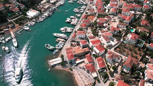 Revealing drone flying over the old harbour revealing piers, boats, turquoise water, houses and landscape of greek Spetses while motorbike is driving on the coastal street photo