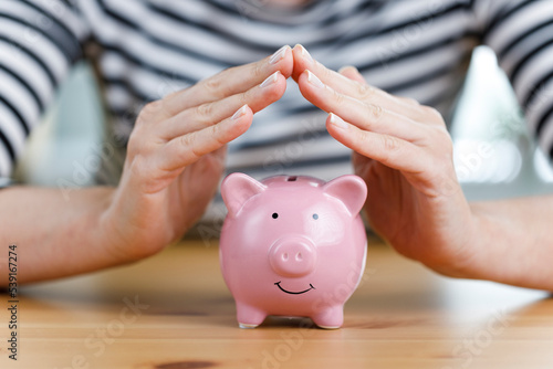 Woman hands covering the pink cute piggy bank. Protect your savings photo