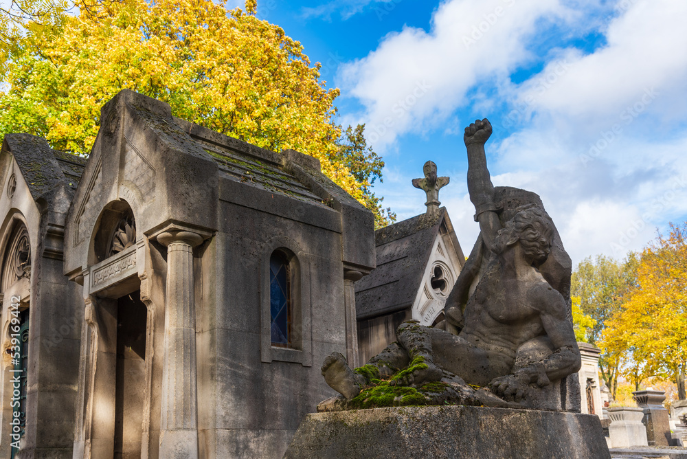 Autumn at  Pere Lachaise cemetery in Paris, France. Antique tombs under blue sky surrounded with golden autumn trees. 