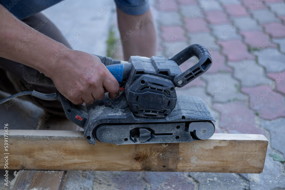 The man's hands are holding a grinding machine. Processing of a furniture part by a machine for polishing a tree. the grinding machine on a board. The man's hands are holding a grinding machine. Processing of a furniture part by a machine for polishing a tree. the grinding machine on a board.