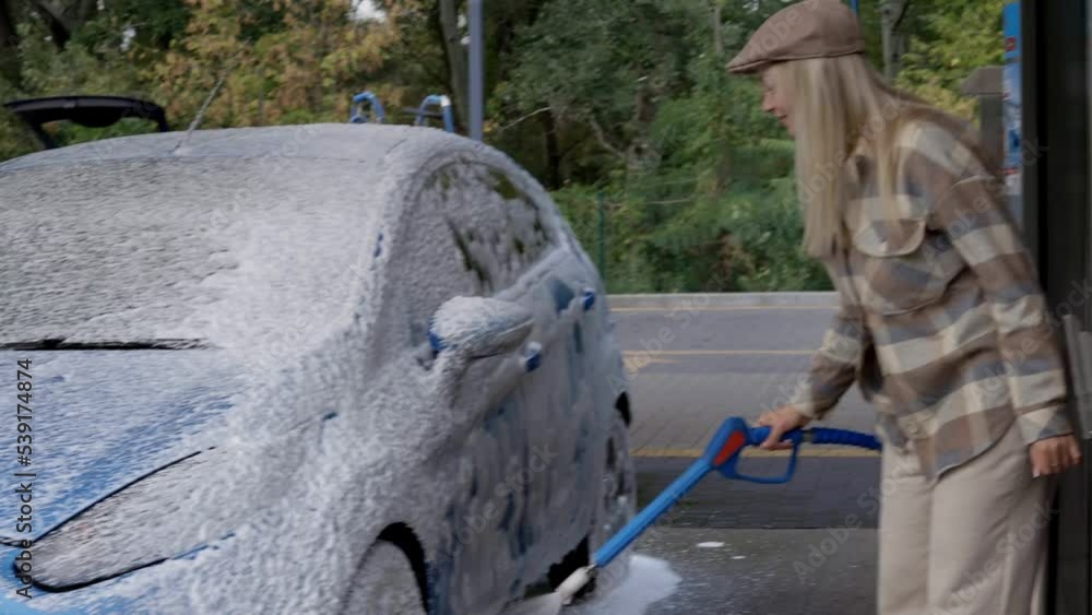 Woman washing a car in a selfservice car wash station with wahing foam