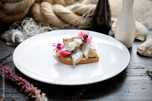 Sandwich with herring and pickled onion, decorated with edible flowers, on a white plate. An elegant fish appetizer.