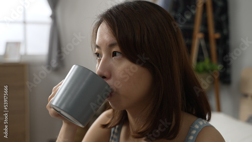 smiling happy beautiful asian woman relaxing drinking hot tea and looking at window. Girl feeling enjoy having breakfast in holiday morning vacation on bed at home. relax female with warm beverage photo