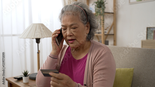half length shot of a asian grey haired senior woman giving credit card details on the mobile phone in the living room at home