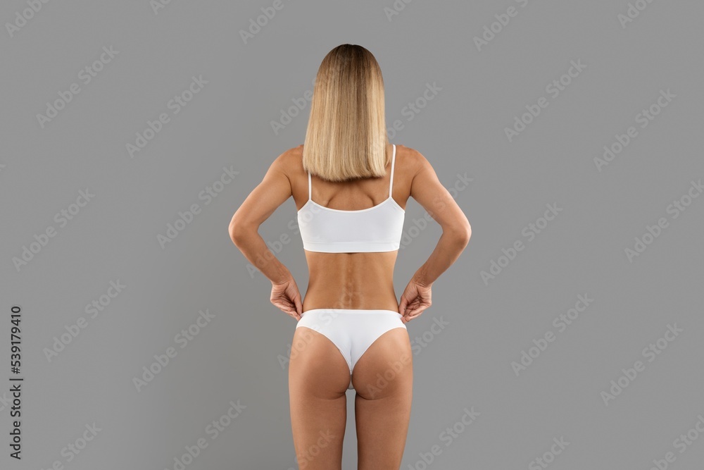 Naklejka premium Rear View Of Slim Young Woman Standing In Underwear On Grey Background