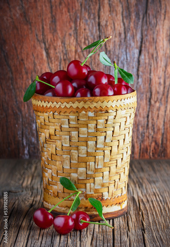 Ripe cherries in a birch bark dish on a wooden table. Green leaves. Photo.
