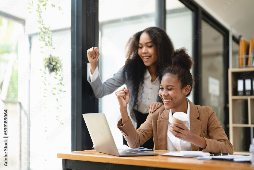 Excited african women achieving goals excited raised hands rejoicing with laptop in the office. New startup project concept. Excited african women achieving goals excited raised hands rejoicing with laptop in the office. New startup project concept.