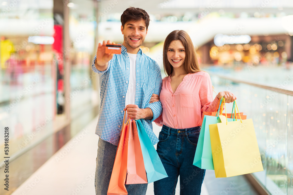 Cheerful Spouses Showing Credit Card Holding Shopper Bags In Mall Cheerful Spouses Showing Credit Card Holding Shopper Bags In Mall