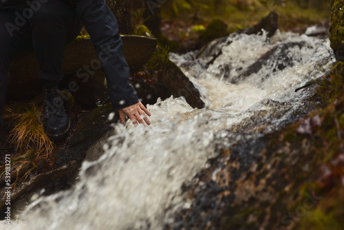 A hand touching water flowing in a stream in a forest.