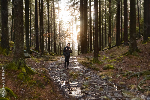 A caucasian man with a backpack walking in a forest on a stone path at sunset.