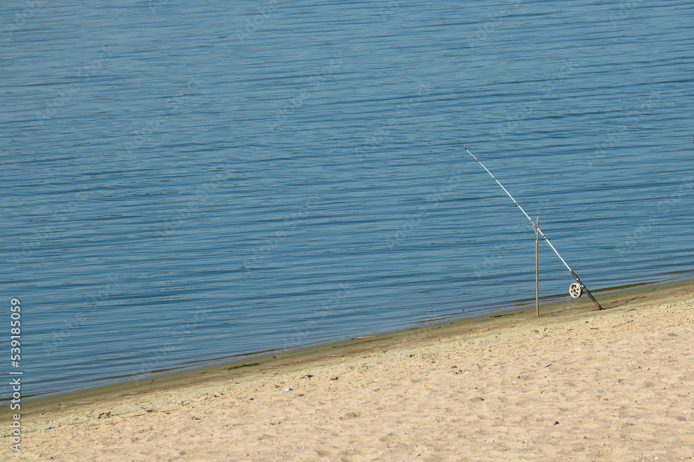 Fishing rod on the sandy shore of a river or lake on a sunny day