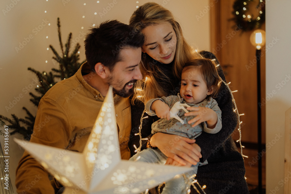 Photo of a family with one child wrapped in Christmas lights, celebrating holidays on their apartment; throwing an unforgettable Christmas party at home.