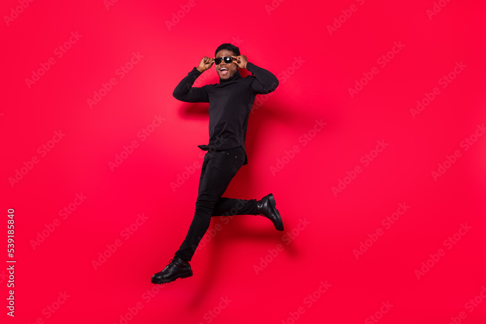 Full length body size view of handsome trendy cheerful guy jumping running touching specs isolated over bright red color background
