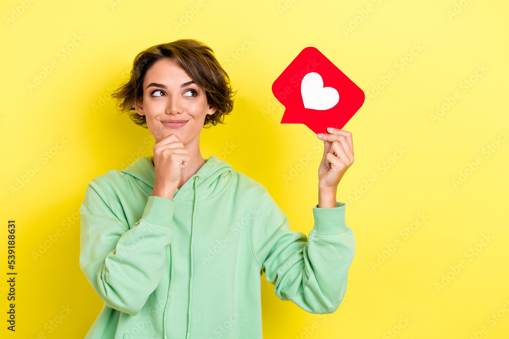 Photo portrait of stunning young woman look curious social media heart icon dressed stylish green look isolated on yellow color background Photo portrait of stunning young woman look curious social media heart icon dressed stylish green look isolated on yellow color background