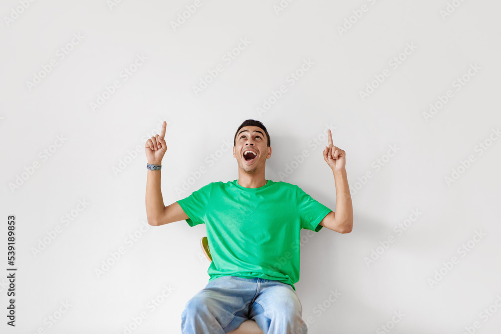 Excited arab man pointing and looking up at copy space, opening mouth in shock on light studio wall background Excited arab man pointing and looking up at copy space, opening mouth in shock on light studio wall background