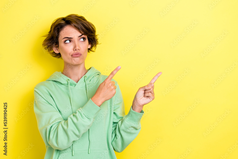 Photo portrait of charming young woman look suspicious point empty space dressed stylish green clothes isolated on yellow color background