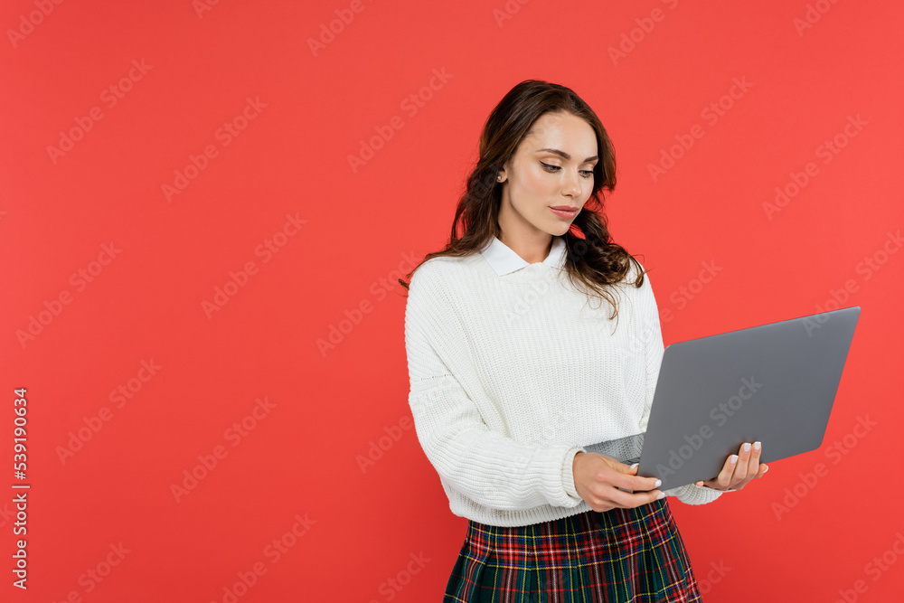 Brunette woman in warm jumper using laptop isolated on red Brunette woman in warm jumper using laptop isolated on red