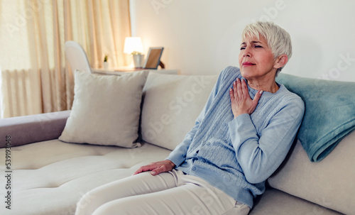 Shot of a senior woman suffering from chest pain while sitting on the sofa at home. Cropped closeup of an mature woman experiencing cardiac discomfort at home. © Jelena Stanojkovic
