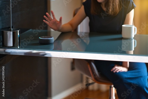 Woman sitting on a chair and talking to a speech recognition device, Amazon Alexa with sunlight background