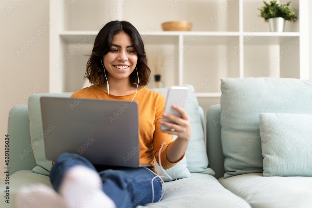 Smiling Young Arab Woman Using Laptop And Smartphone While Resting At Home Smiling Young Arab Woman Using Laptop And Smartphone While Resting At Home