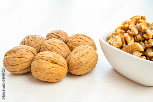 Walnuts in shell next to bowl containing shelled walnuts. Pruduction and consumption of nuts. Nutrition and properties of walnuts.
 photo