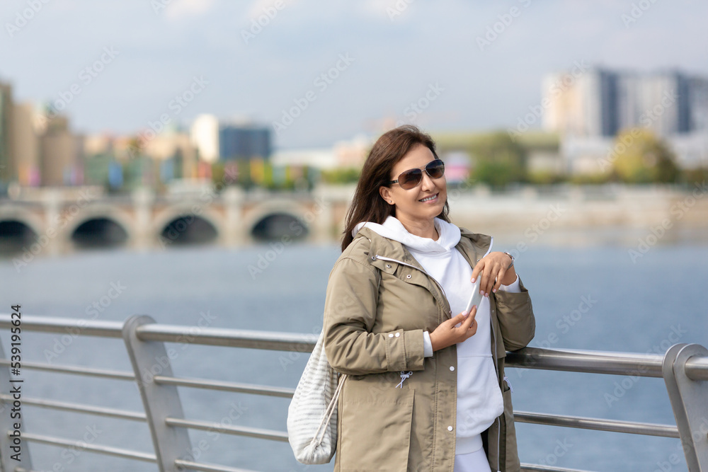 Attractive smiling Caucasian woman plus size in stylish outfit stands on the city embankment, selective focus.