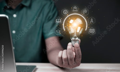 Businessman holding glowing lightbulb with learning icons for study knowledge to creative thinking idea and problem solving solution concept.