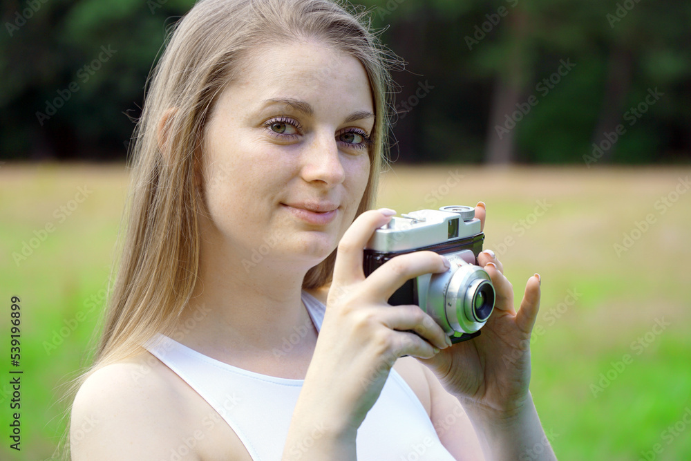 Young woman taking pictures with vintage photo camera in nature on a sunny summer day