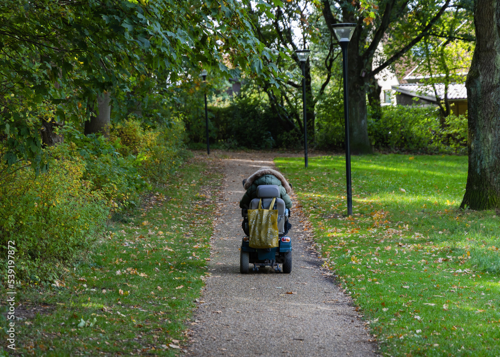 A woman in a wheelchair is driving along the road to the parks. A woman in a wheelchair is driving along the road to the parks.