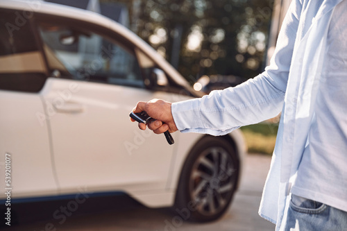 Standing with keys and locking the automobile. Close up view of man with his electric car