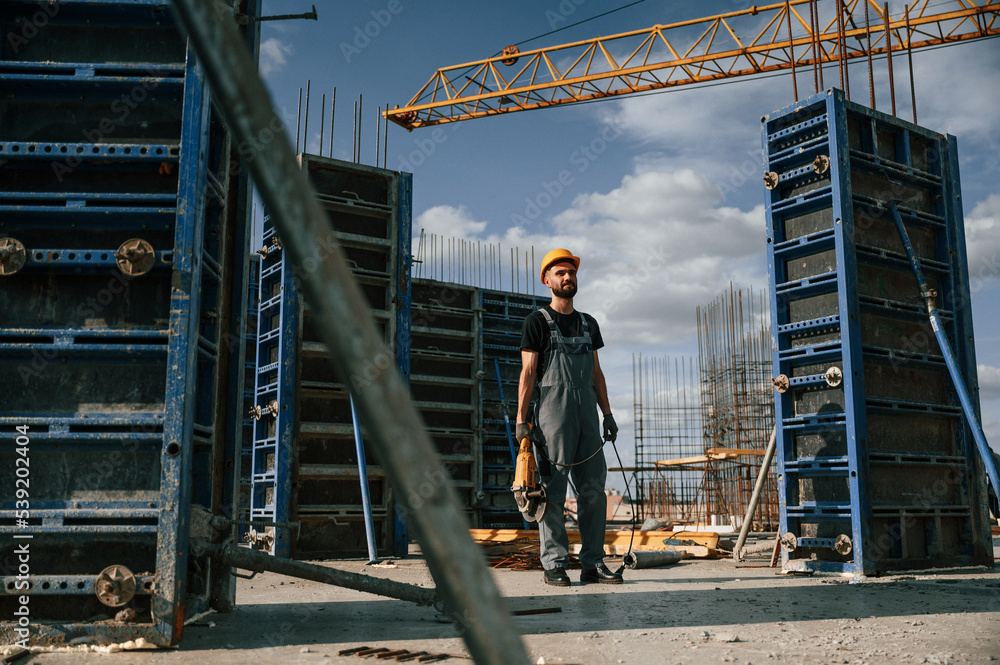 Standing with grinding machine in hands. Man in uniform is working on the construction site Standing with grinding machine in hands. Man in uniform is working on the construction site