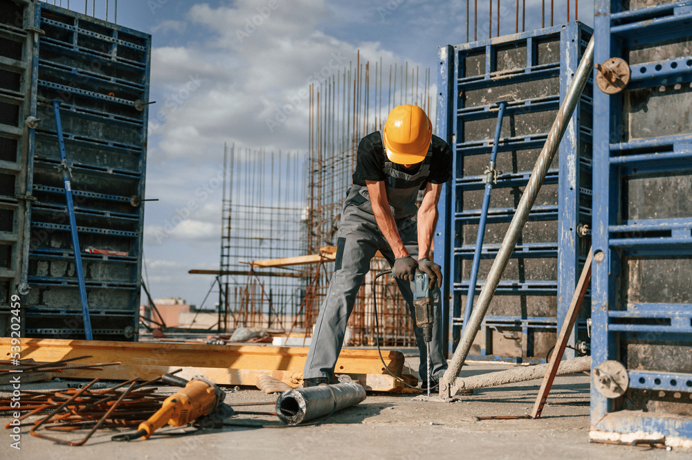 Using the drill. Man in uniform is working on the construction site Using the drill. Man in uniform is working on the construction site