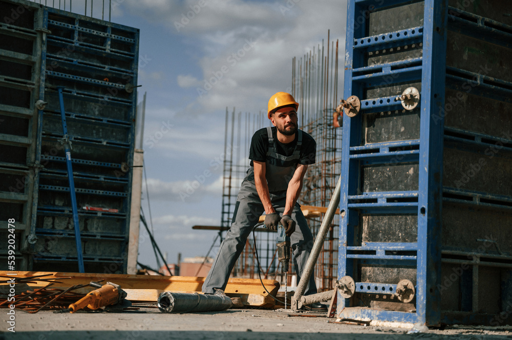 Using the drill. Man in uniform is working on the construction site Using the drill. Man in uniform is working on the construction site
