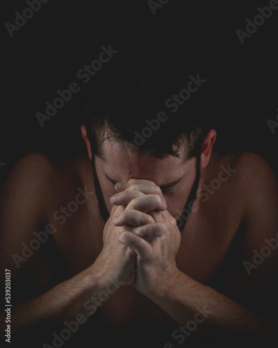 Fotografie bearded man laying head on hands or praying with black background