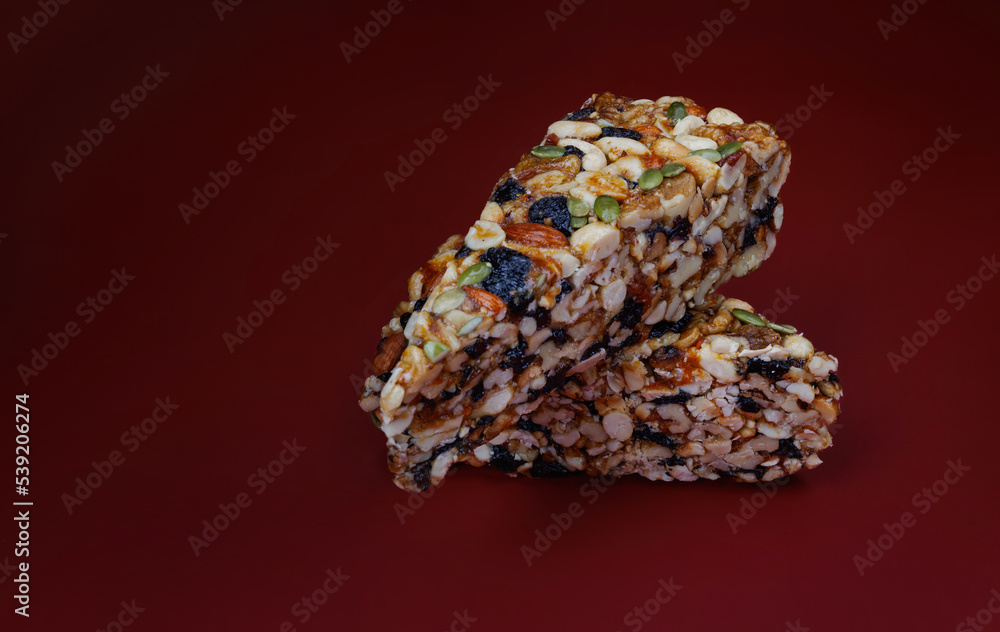 Two pieces of gozinak from various nuts with dried fruits on a red background. Two pieces of gozinak from various nuts with dried fruits on a red background.