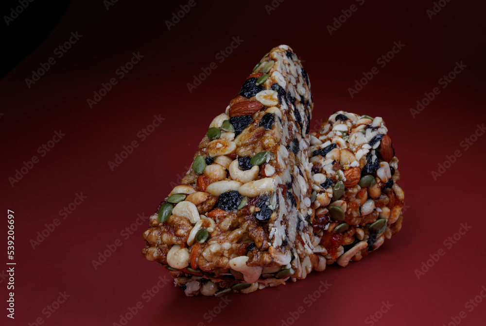 Two pieces of gozinak from various nuts with dried fruits on a red background. Two pieces of gozinak from various nuts with dried fruits on a red background.