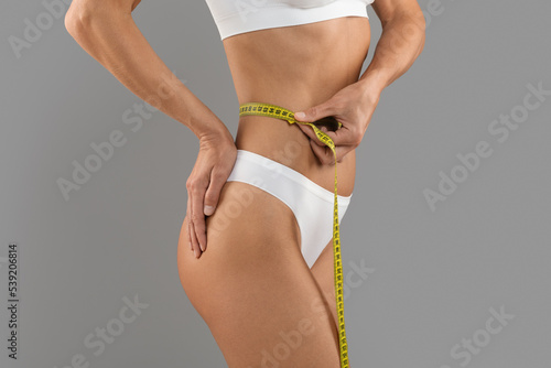 Young Slim Female In White Underwear Measuring Her Waist With Yellow Tape